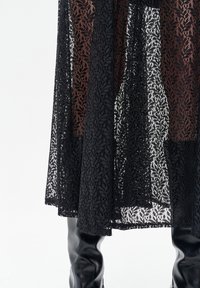 Zwarte kanten rok met ingewikkelde bloemenpatronen, semi-transparante textuur en een vloeiende snit, gecombineerd met nauwsluitende zwarte laarzen tot aan de knie.