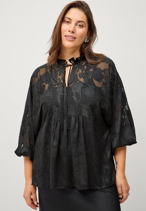Sort gennemsigtig bluse med blomsterbroderi, der har en bundet krave, bløde ærmer og en samlet talje, hvilket skaber en afslappet silhuet.
