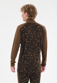 Braunes Langarmshirt mit schwarzen Textmustern auf der Rückseite und einfarbigen braunen Ärmeln. Weicher Stoff mit taillierter Passform.