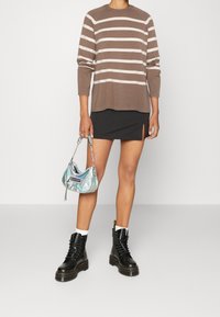 Pull rayé brun et crème, mini-jupe noire avec une fente sur le côté, sac à main irisé, et bottines noires à lacets avec semelles épaisses.