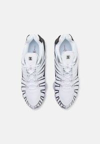 Baskets de sport blanches avec un dessus en maille, des accents noirs, un bout arrondi et une texture en relief unique sur les côtés. Fermeture à lacets.