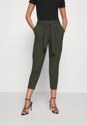 Woman wearing high-waist olive green cropped pants with a belt, black short sleeve top, and black strappy high heels.
