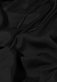 Tessuto nero con una superficie liscia, caratterizzato da un cordoncino e morbidi drappeggi fluidi, che mostrano una sottile riflessione della luce.