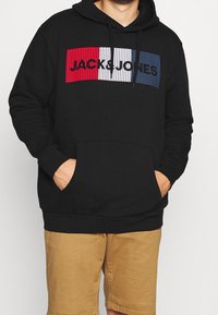 Černá mikina s kapucí s výrazným panelem v červené, bílé a modré barvě s nápisem „JACK&JONES“, měkká tkanina a kapsa vpředu.