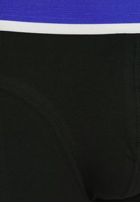 Svart underklädnad med ett elastiskt midjeband i blått och vitt. Slät textur med stickade detaljer och en figurnära design.