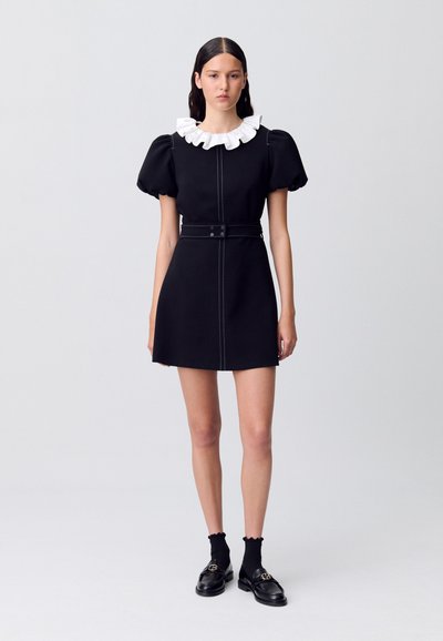 Vestido negro con mangas abullonadas, cuello blanco con volantes, cremallera frontal y cintura con cinturón. Combinado con calcetas negras y mocasines. Tejido suave.