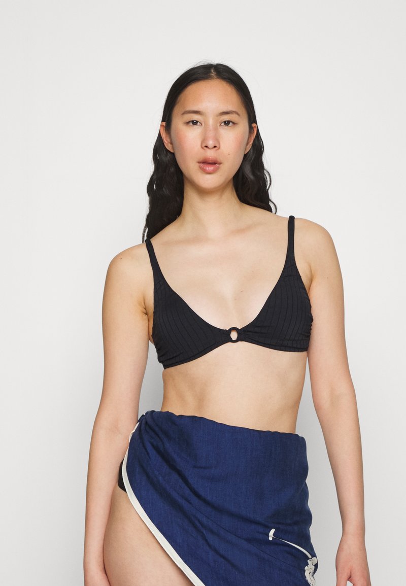 Top de bikini preto com textura canelada em forma triangular e um destaque circular no centro, combinado com uma saia envolvente azul com um acabamento branco.