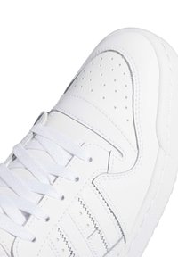 Hvide sneakers med en glat læderoverdel med perforerede sektioner, flade hvide snørebånd og syet detaljer langs kanterne.