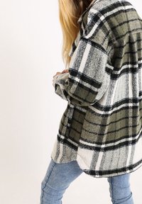 Camicia di flanella a quadri in verde, nero e bianco. Presenta una vestibilità comoda, chiusura a bottoni e una consistenza morbida. Maniche lunghe, orlo arrotondato.