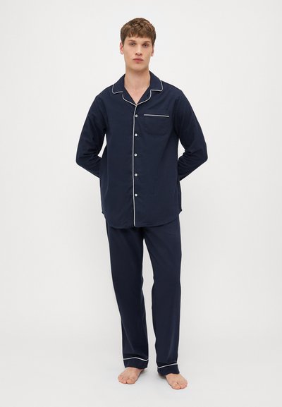 Conjunto de pijama em algodão azul-marinho com detalhes em branco; blusa de botão de mangas compridas com um bolso, combinada com calças ajustadas iguais.