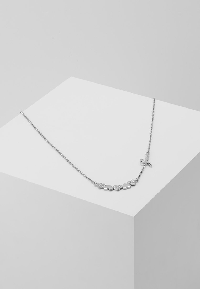 Collier en argent avec sept petits cœurs liés, certains incrustés de minuscules pierres, présenté sur un piédestal géométrique blanc.