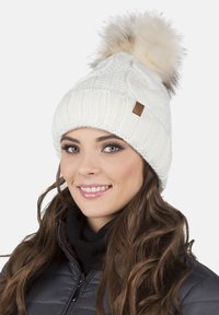 White knitted beanie with a textured pattern, featuring a large faux fur pom-pom on top and a small leather tag on the side.