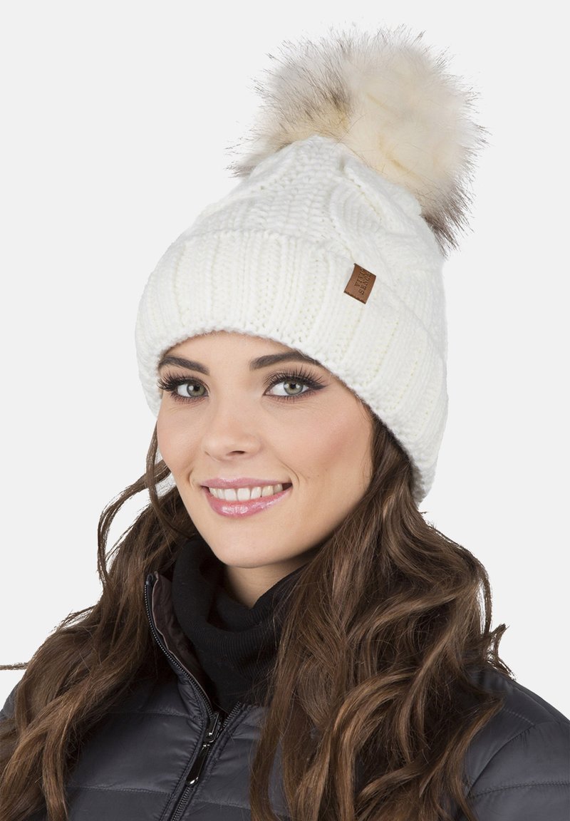 White knitted beanie with a textured pattern, featuring a large faux fur pom-pom on top and a small leather tag on the side.