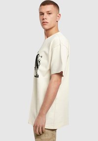 Cremefarvet bomulds T-shirt med korte ærmer, med et sort grafisk print på forsiden og et afslappet fit design.