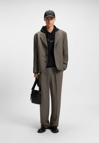 Brown tailored suit with matching trousers, black hooded sweatshirt, black cap, and a small crossbody bag, featuring a smooth texture.