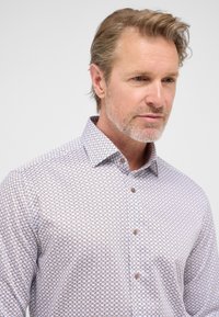 Witte knop-up shirt met een klein, herhalend blauw en paars patroon. Bevat een puntig kraag en bruine knopen aan de voorkant.