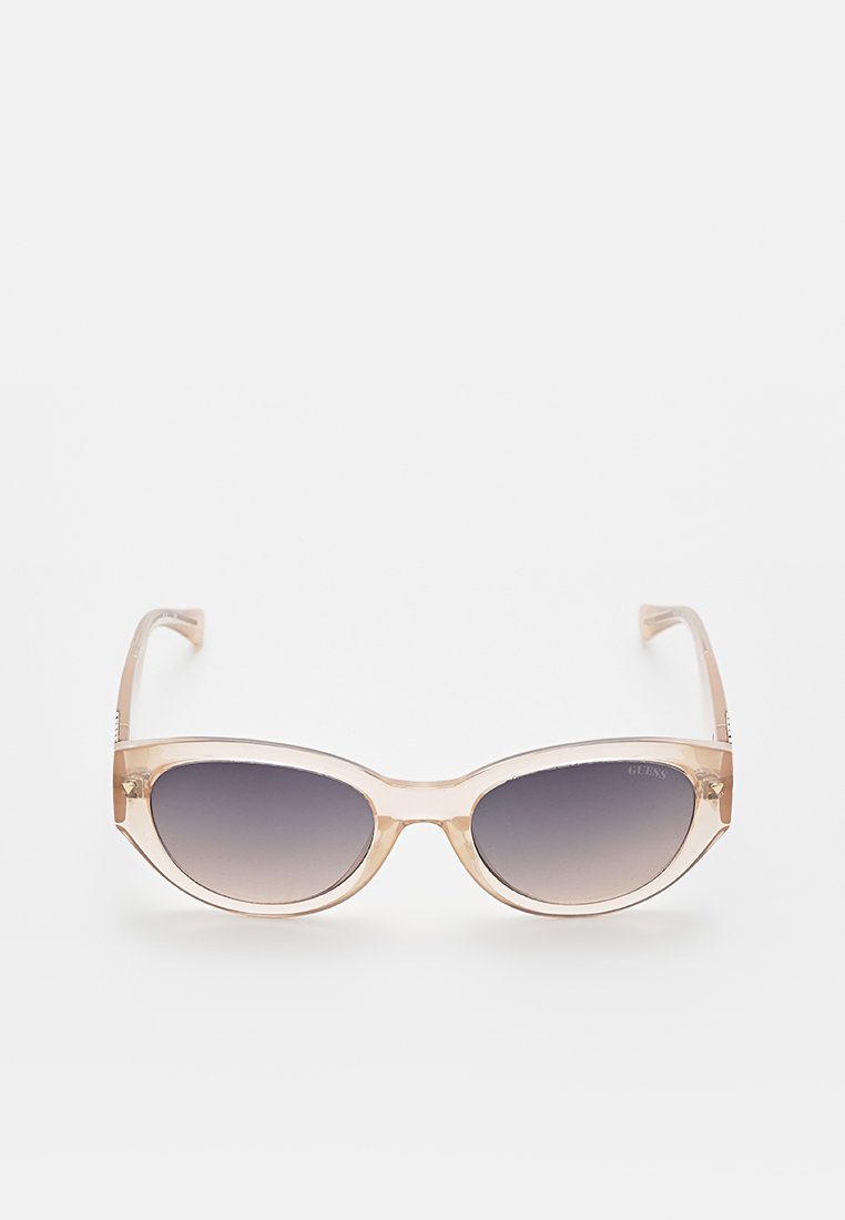 Transparente beigefarbene Katzenaugen-Sonnenbrille mit dunklen Verlaufslinsen, präsentiert vor einem weißen Hintergrund.