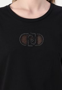 T-shirt nera in cotone con design in rete e strass nella zona del petto, dotata di scollatura rotonda e maniche corte.