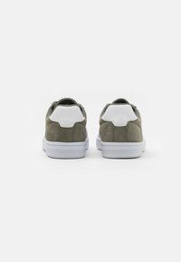 Grønne semskede sneakers med hvite lærhælakkenter. Har en avrundet form og gummisåler. Designet er enkelt og moderne.