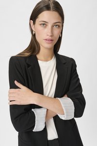 Melnā žakete ar pieguļošu piegriezumu, ar manšetes piedurknēm vieglā svītru rakstā, pāri baltai krekla. Gluda auduma tekstūra.
