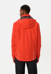 Rode waterdichte jas met capuchon, mesh voering en verstelbare manchetten. Kenmerkt zich door witte accenten en branding op de onderrug.