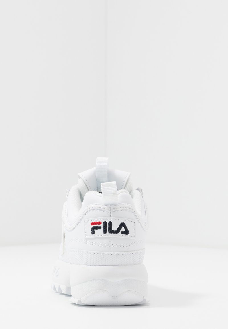 Zapatilla atlética blanca con una parte superior texturizada, que presenta un logotipo, un cuello acolchado y una suela de goma gruesa con un patrón irregular.