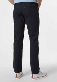 Ciemnoniebieskie bawełniane spodnie o prostym kroju, z dwoma tylnymi kieszeniami i srebrnymi detalami. Noszone z jasnymi butami.