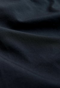 Prim-plan cu țesătură netedă, bleumarin închis, cu pliuri moi și textură subtilă vizibilă în lumina.