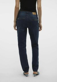 Jeans de denim azul oscuro con un diseño de pierna recta, sutiles bolsillos traseros y un parche de cuero marrón en la cintura. Textura suave.
