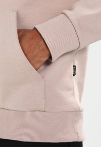 Felpa beige chiaro con polsini e orlo a costine, dotata di una tasca laterale. L'etichetta recita "CHASIN". Il tessuto sembra morbido e testurizzato.