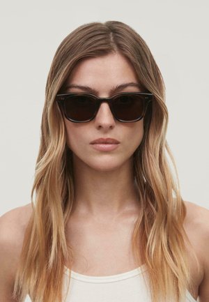 Lunettes de soleil noires rectangulaires avec des verres foncés, dotées d'une monture en plastique épaisse et de subtils accents de logo sur les branches.