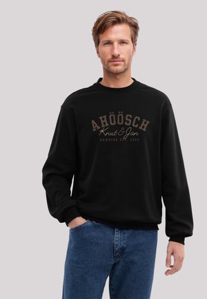 Schwarzer Pullover aus Baumwolle mit rundem Ausschnitt und langen Ärmeln. Vorderseite mit braunem Text, der die Worte "AHÖÖSCH Knut & Jan" zeigt.