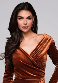 Robe en velours d'un riche brun orangé avec un col drapé et des manches longues. Présente un détail froncé à l'épaule et des boucles d'oreilles élégantes.