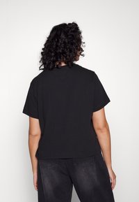 Camiseta de algodón negra con mangas cortas y un ajuste holgado, que presenta un cuello redondo y una textura suave. La vista trasera no muestra detalles adicionales.