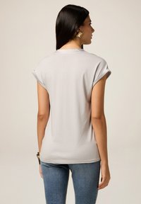T-shirt grigio chiaro a maniche corte con risvolti e vestibilità rilassata, realizzato in un morbido tessuto elasticizzato, abbinato a jeans blu.