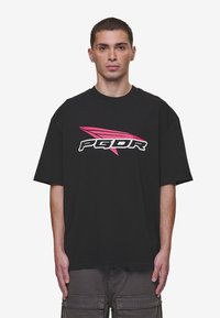 Black oversized t-shirt made of cotton, featuring a bold pink and white "PGDR" logo with an angled design across the chest.