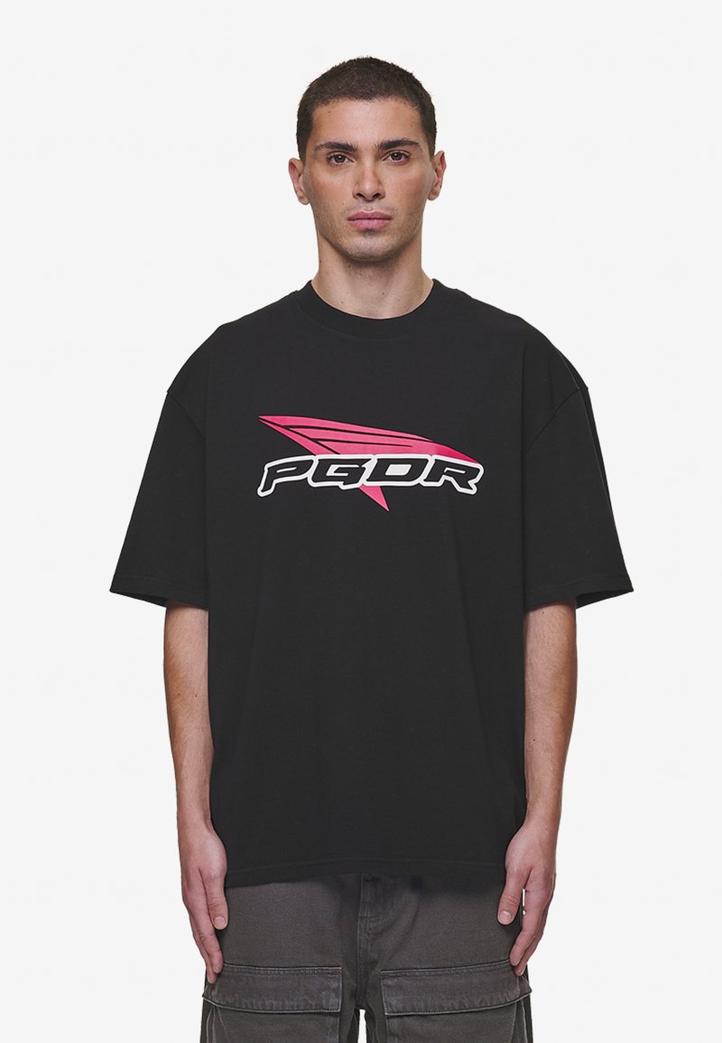 Črna oversized majica iz bombaža, ki ima drzen roza in belo "PGDR" logo z naklonskim dizajnom čez prsi.