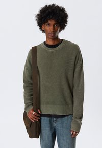 Green knit sweater with a textured pattern, paired with a black undershirt, light blue jeans, and a brown shoulder bag.