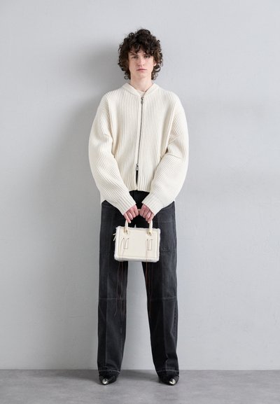 Cream ribbed zip-up sweater, loose fit; black wide-leg pants with seam details; small white handbag with top handles.