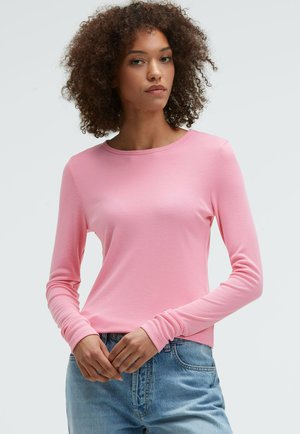 Langärmliges pinkes Oberteil aus einem weichen, dehnbaren Stoff mit rundem Halsausschnitt und taillierter Silhouette, kombiniert mit hellblauen Jeans.