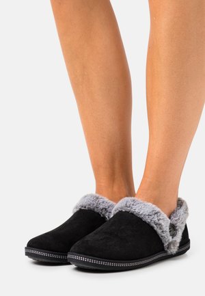 Zwarte suède pantoffels met een grijze bontafwerking, instapontwerp, ronde neus en decoratieve stiksels langs de zool. Accentueert met een knoopdetail.