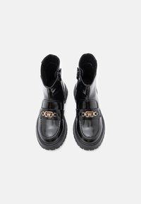Bottines en cuir verni noir avec semelles épaisses, zips latéraux et détail en chaîne dorée sur les sangles avant, vues de dessus.