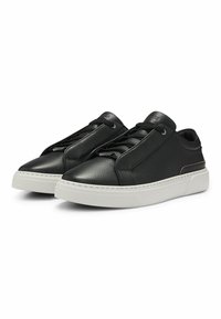 Un par de zapatillas de cuero negro texturizado con cordones negros y suelas gruesas de goma blanca, inclinadas hacia la izquierda sobre un fondo blanco.