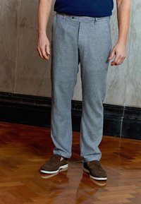 Grå, strukturerede bukser med skræddersyet pasform, der har for-pleats og flad front. Kombineret med mørkebrune, ruskinds loafers på trægulv.