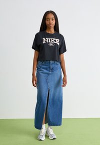 Zwart crop t-shirt met "NIKE" logo, hoge taille denim rok met een split aan de voorkant, blauwe tint, gedragen met witte sneakers en enkel sokken.