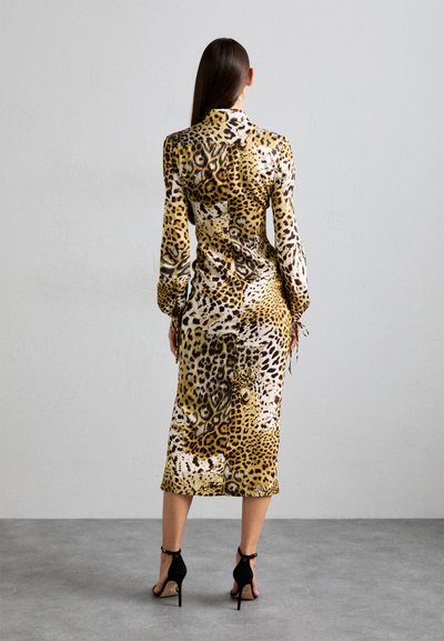 Long-sleeved, form-fitting dress with a leopard print in shades of yellow and brown, featuring a belted waist and button details at the back.