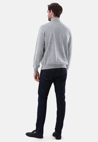 Grauer gestrickter Pullover mit hohem Kragen, gerippten Bündchen und lässiger Passform, kombiniert mit dunkelblauen Jeans und schwarzen Slippern.