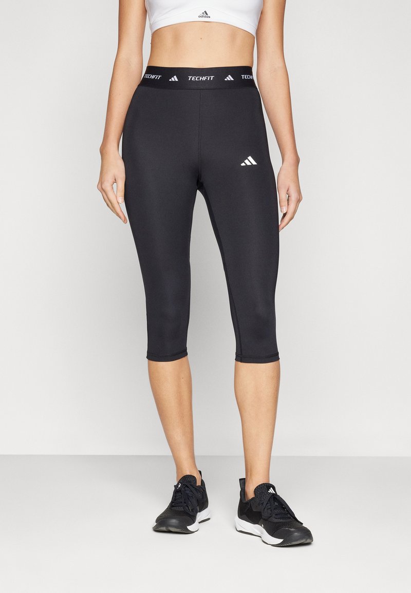Leggings capri atletici neri con branding TechFit, presentano un design a taglio aderente e una texture liscia, completati da accenti bianchi del logo.