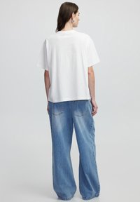 Witte katoenen T-shirt met korte mouwen, gecombineerd met lichtblauwe, wijde denim jeans met achterzakken en een zachte textuur.