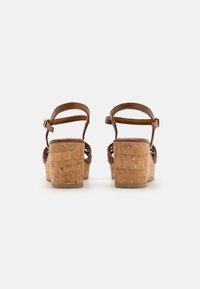 Sandali in sughero con cinturino in pelle marrone e dettagli intrecciati. Il tacco è spesso e texturizzato, offrendo una finitura naturale.